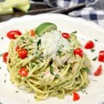 Green spaghetti with chopped tomatoes and parmesan cheese on a plate.