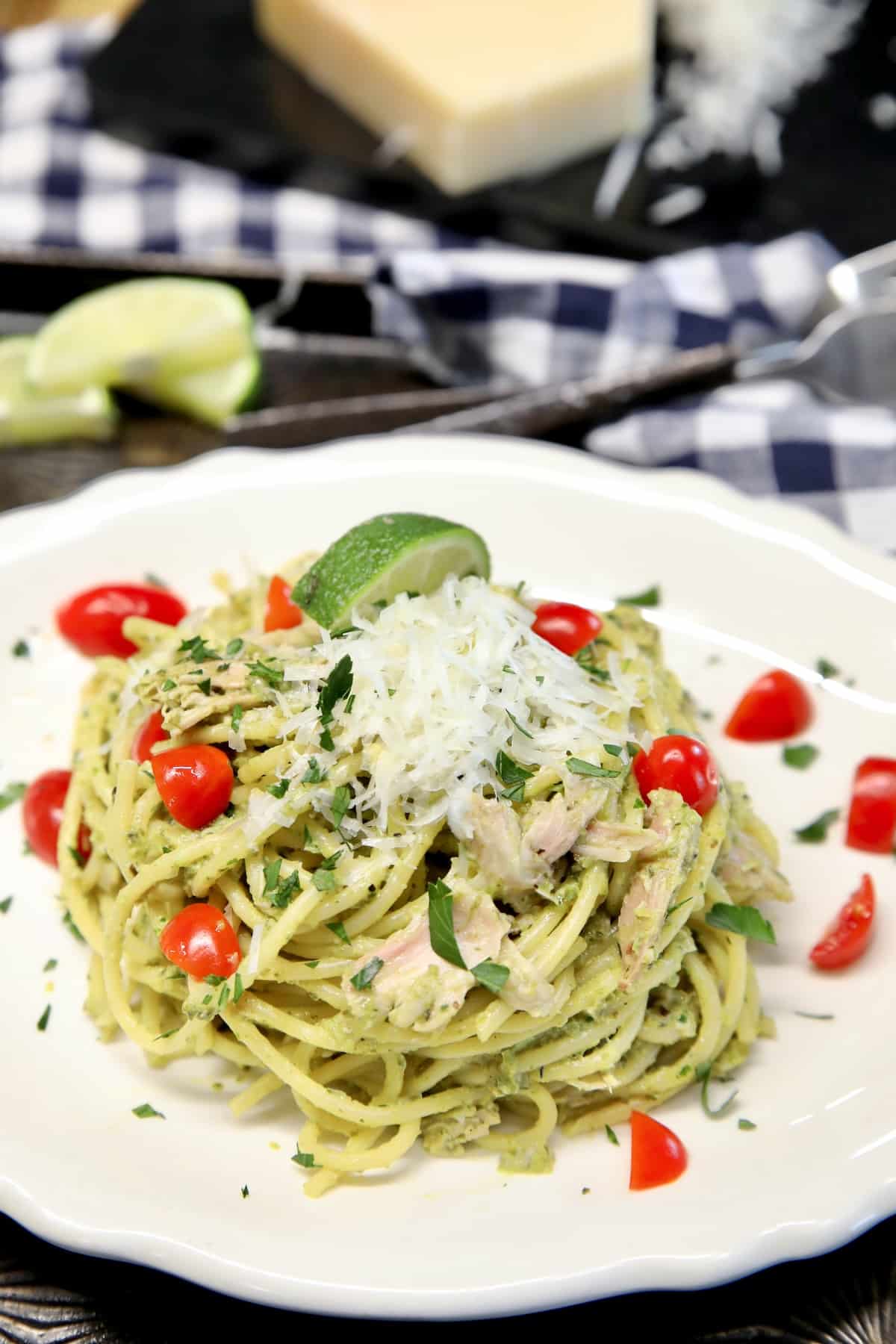 Plate of green spaghetti with chicken, tomatoes, parmesan.