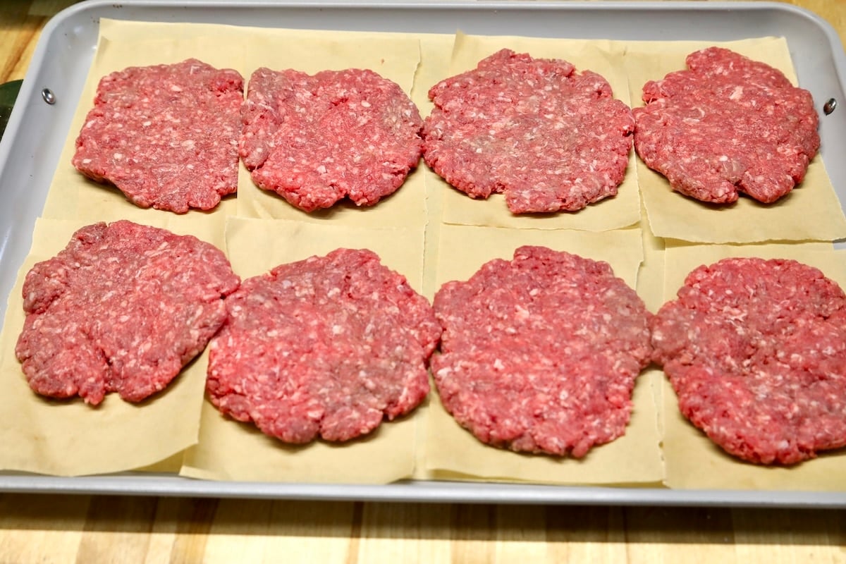 Burger patties on a parchment lined baking sheet.