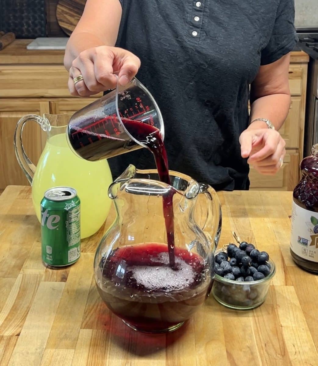 Pouring blueberry juice into a pitcher.