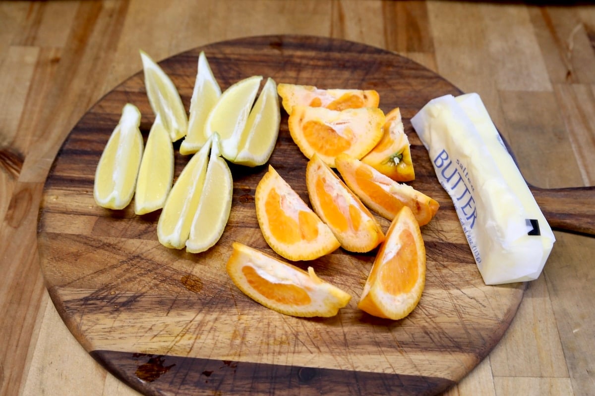 Orange and lemon slices on a cutting board with stick of butter.