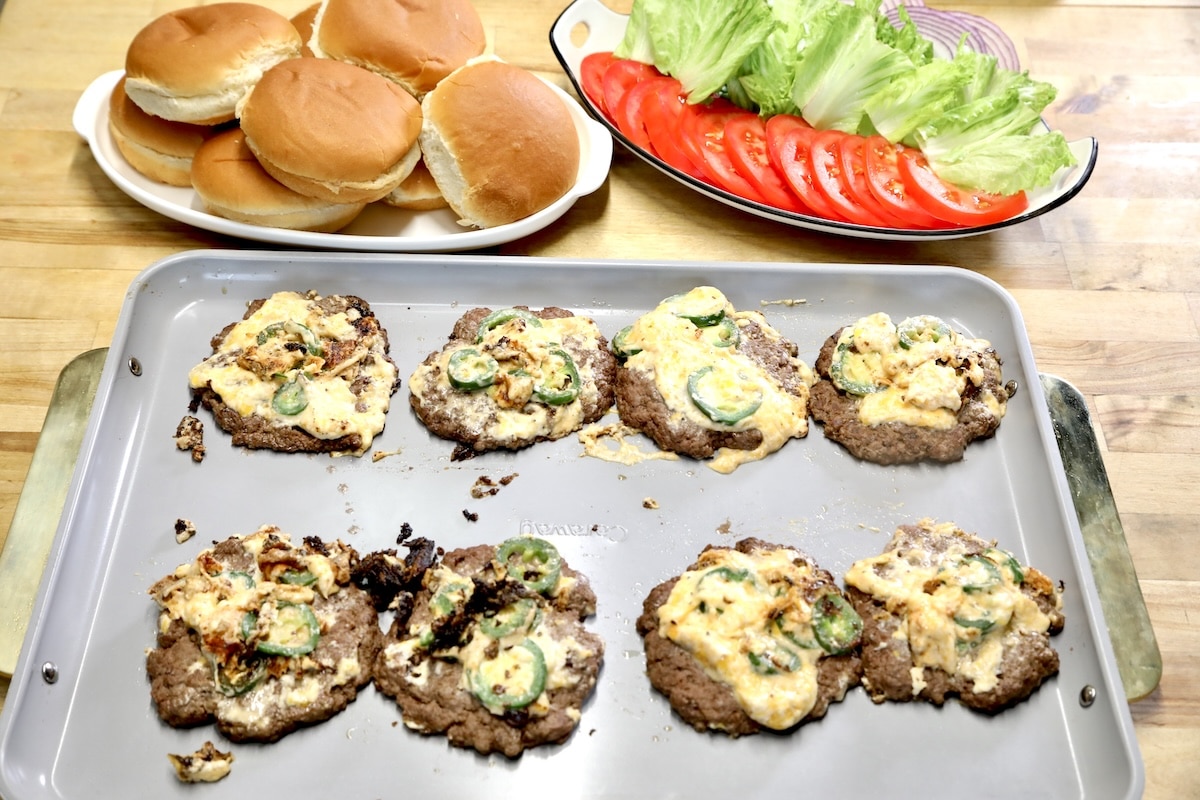 Jalapeno popper burger patties on platter, buns, toppings in background.