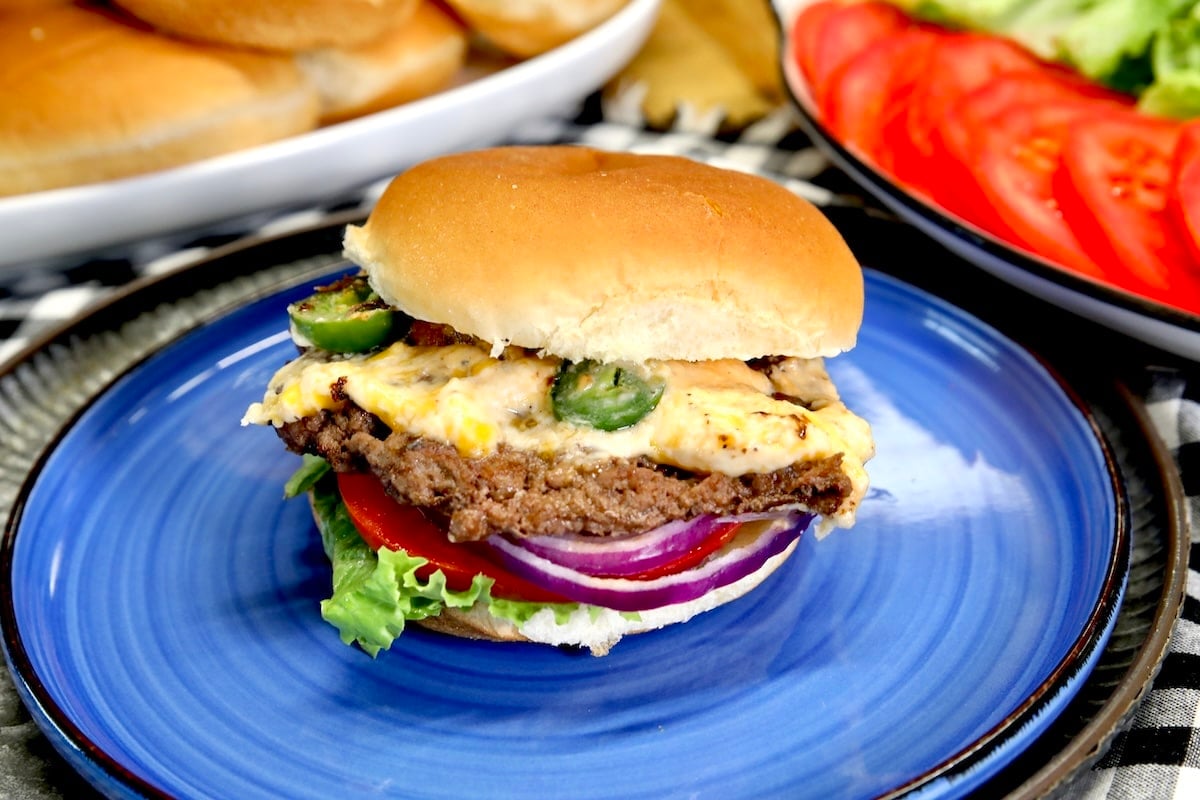 Burger with jalapeno popper topping on a blue plate.