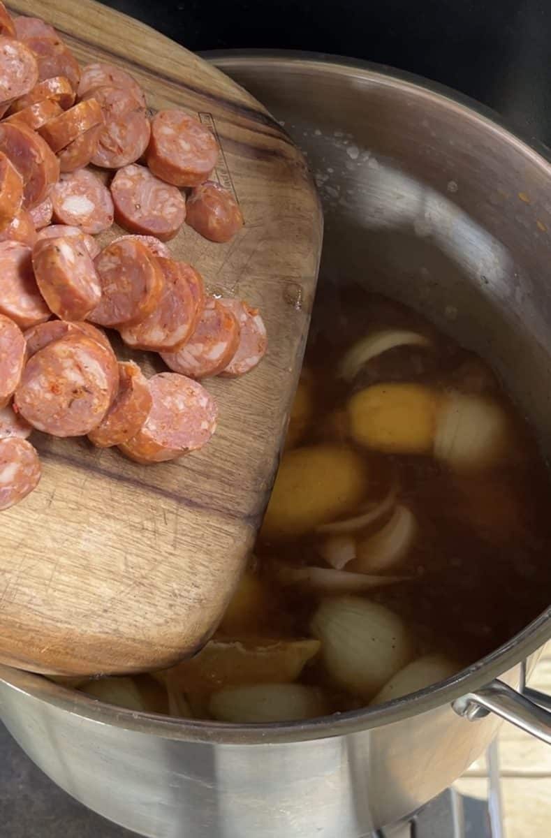 Adding smoked sausage to a stock pot.