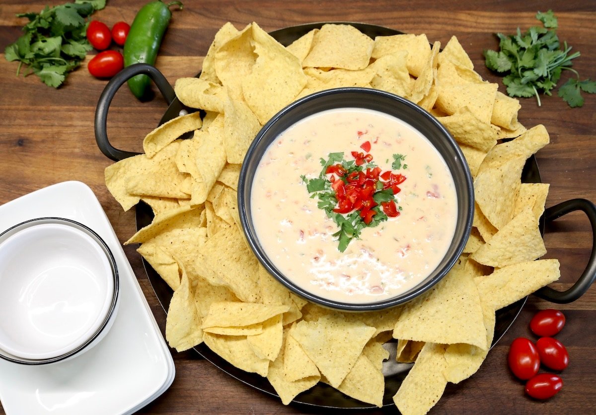 Platter of tortilla chips with white cheese dip, bowls and plates.