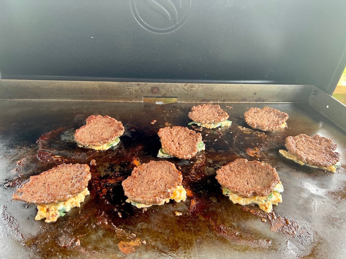 Griddle burgers cooking cheese side down.
