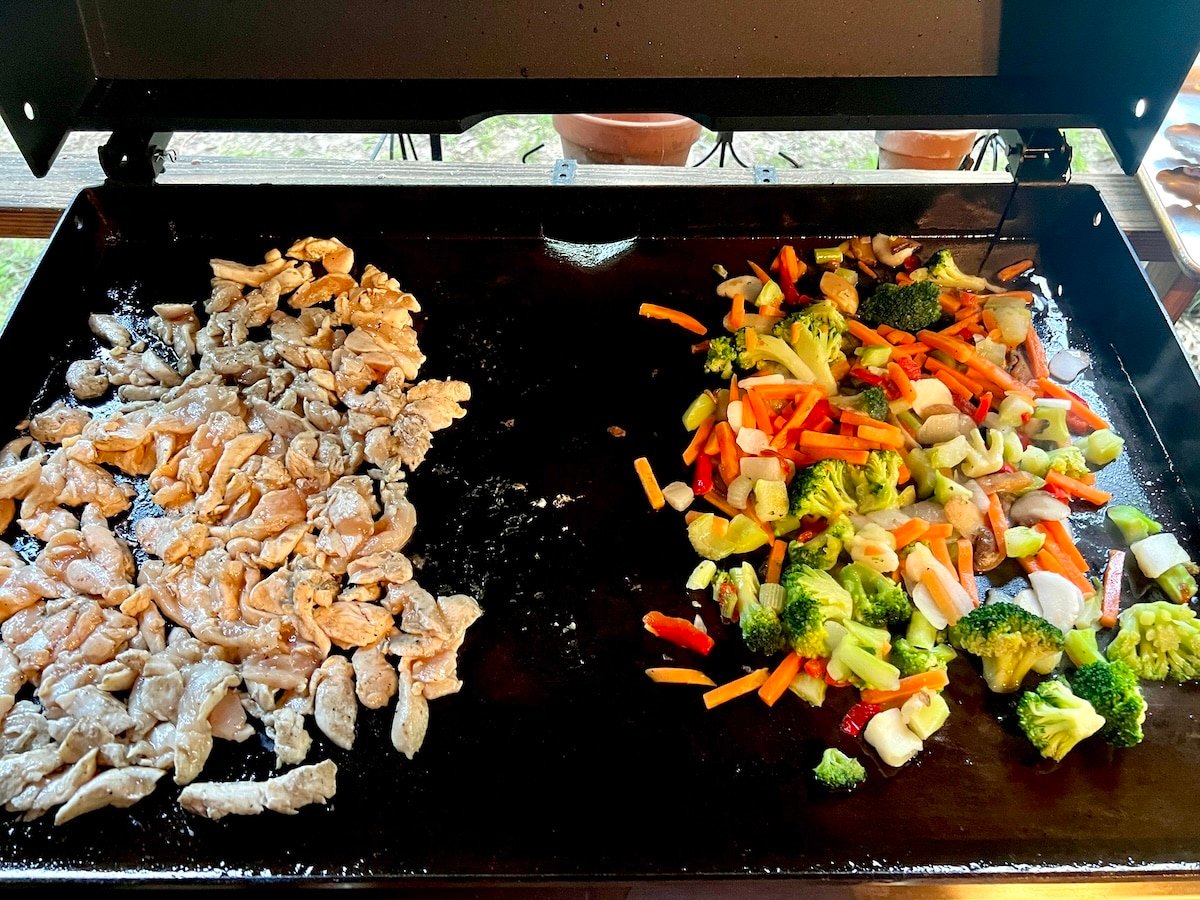 Blackstone chicken and vegetable stir fry. Blackstone griddle with chicken on one side, stir fry vegetables on the other.