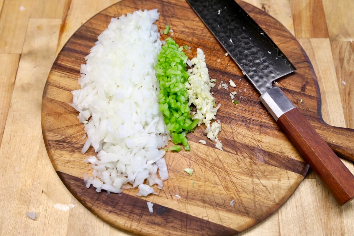 Cutting board with diced onion, jalapeno, garlic and a knife.