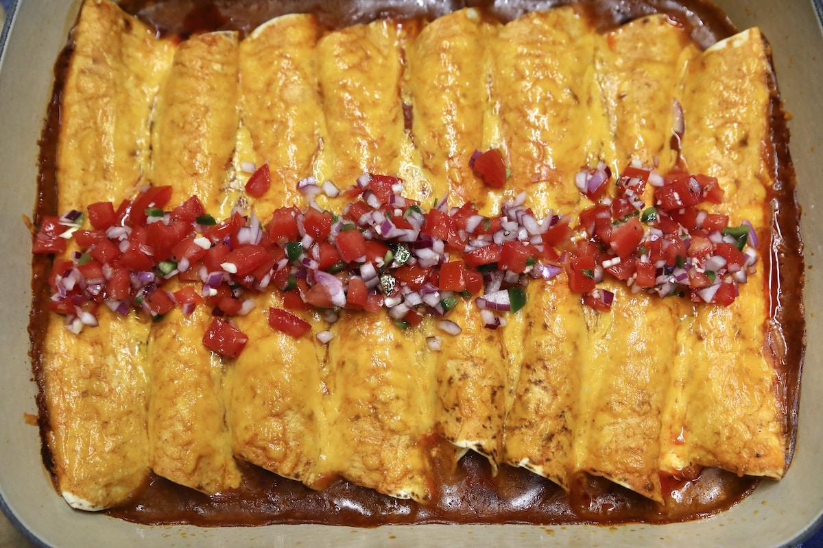 Shredded beef enchiladas in a pan topped with pico de gallo.