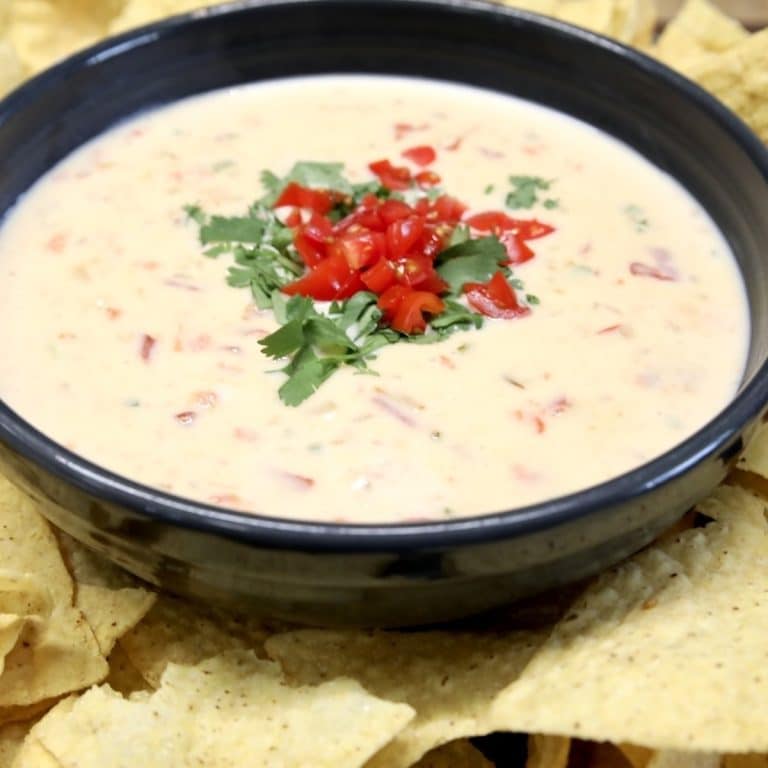 Bowl of white cheese dip with diced tomatoes and cilantro garnish.