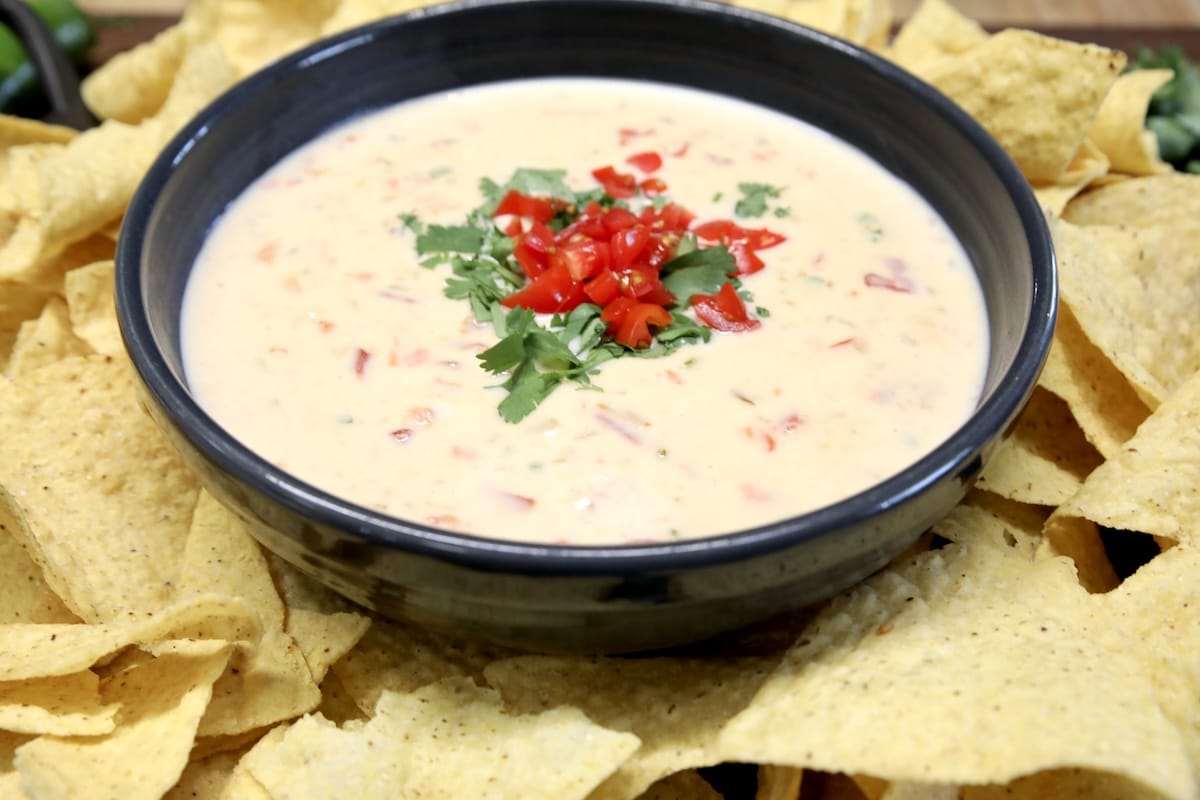 White Velveeta cheese dip. White cheese dip in a black bowl with tomato and cilantro garnish - chips around the bowl.