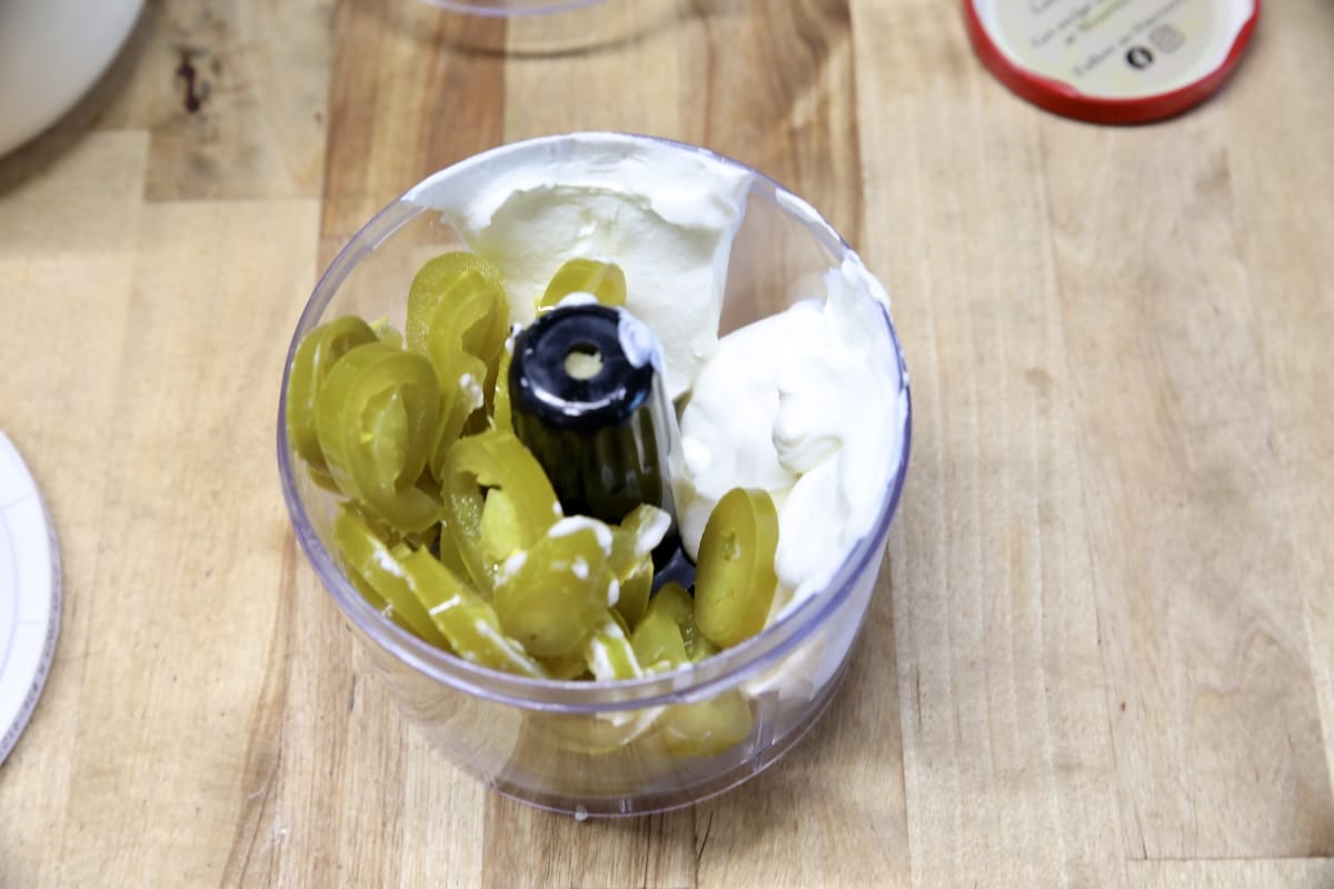 Food processor bowl with sour cream and sliced jalapenos.