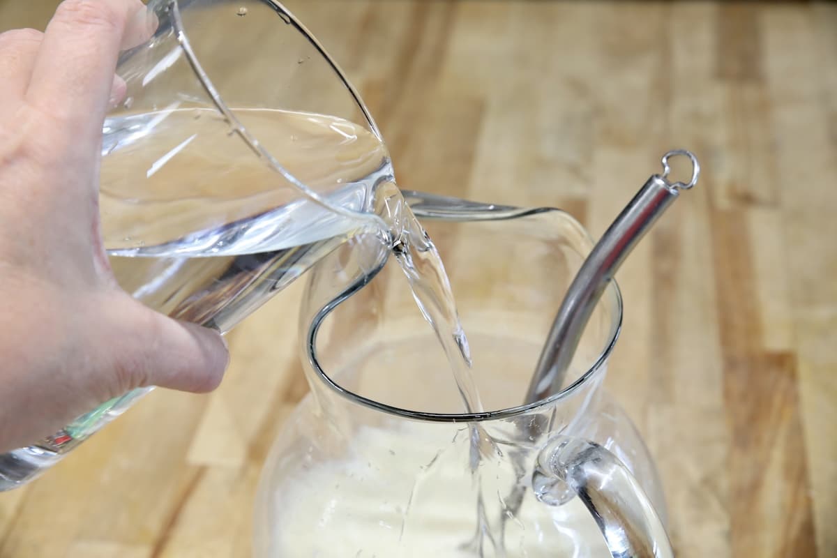 Pouring water into pitcher for homemade lemonade.