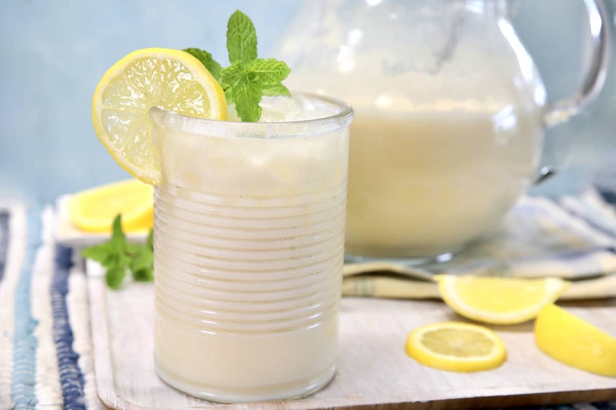 Creamy Lemonade in a glass with pitcher behind.