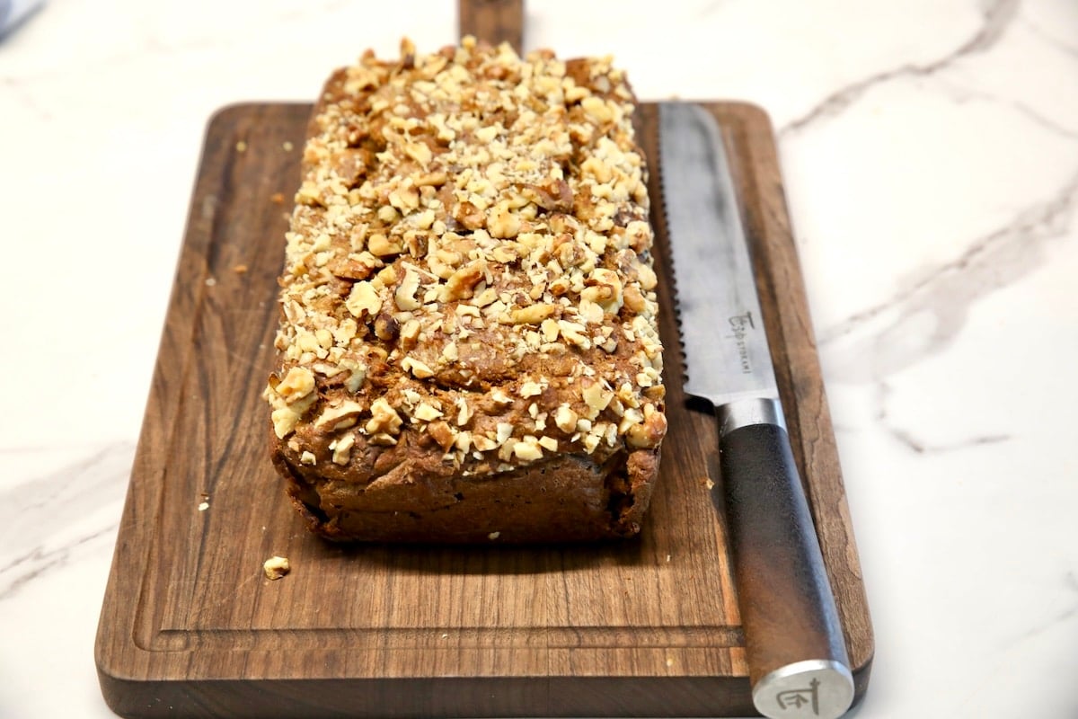 Banana walnut bread loaf with knife on cutting board.
