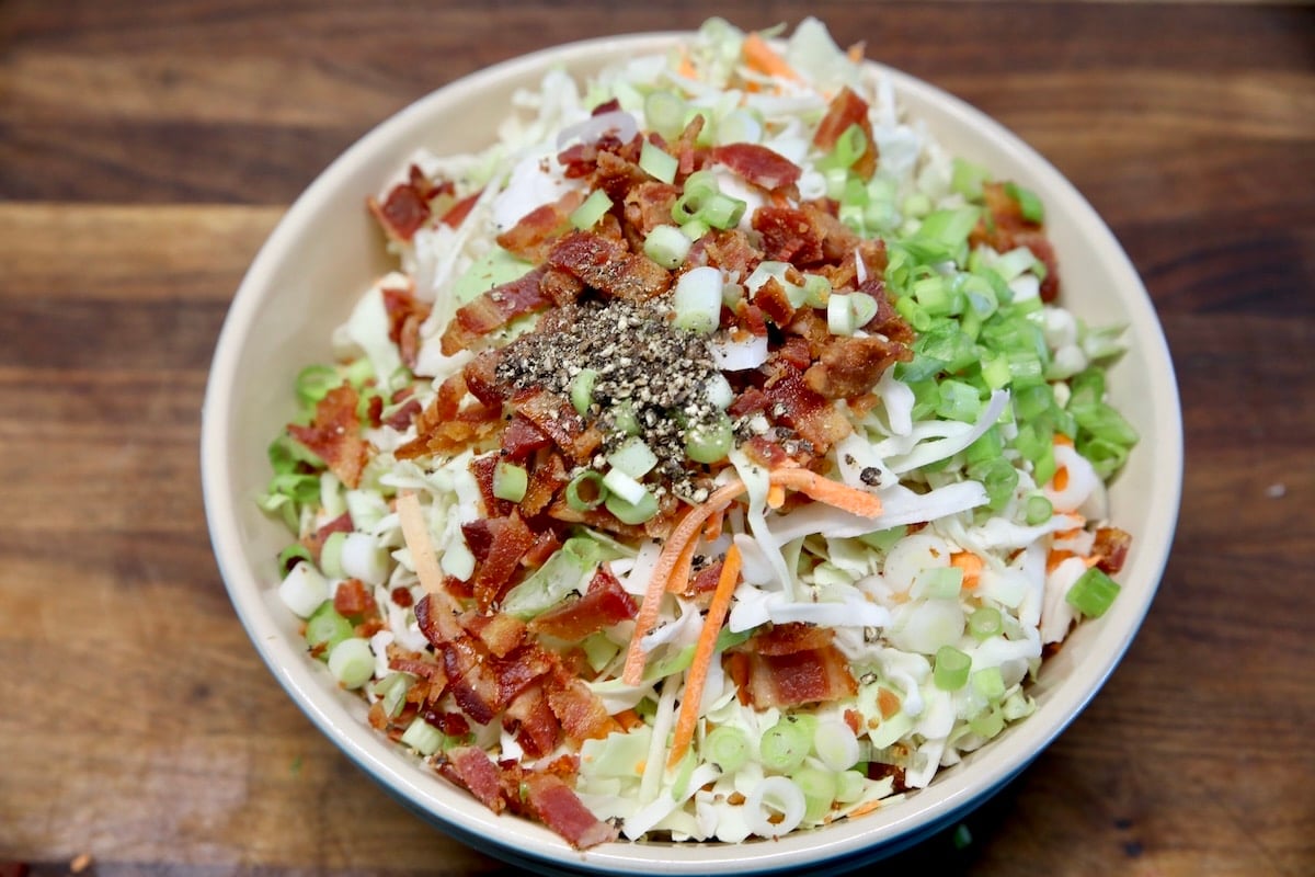 Coleslaw mix in a bowl with bacon and green onions.