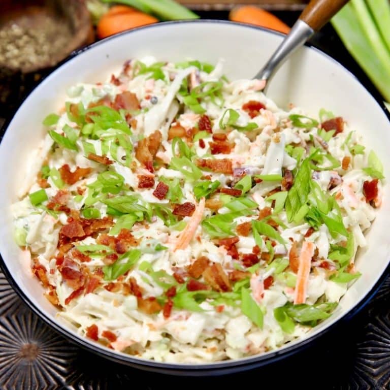 Bowl of coleslaw with bacon and green onions.