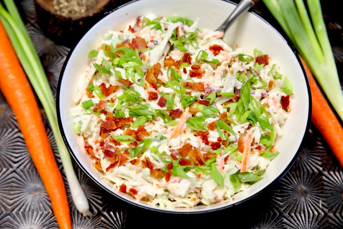 Bacon ranch coleslaw with carrots and green onions next to the bowl.