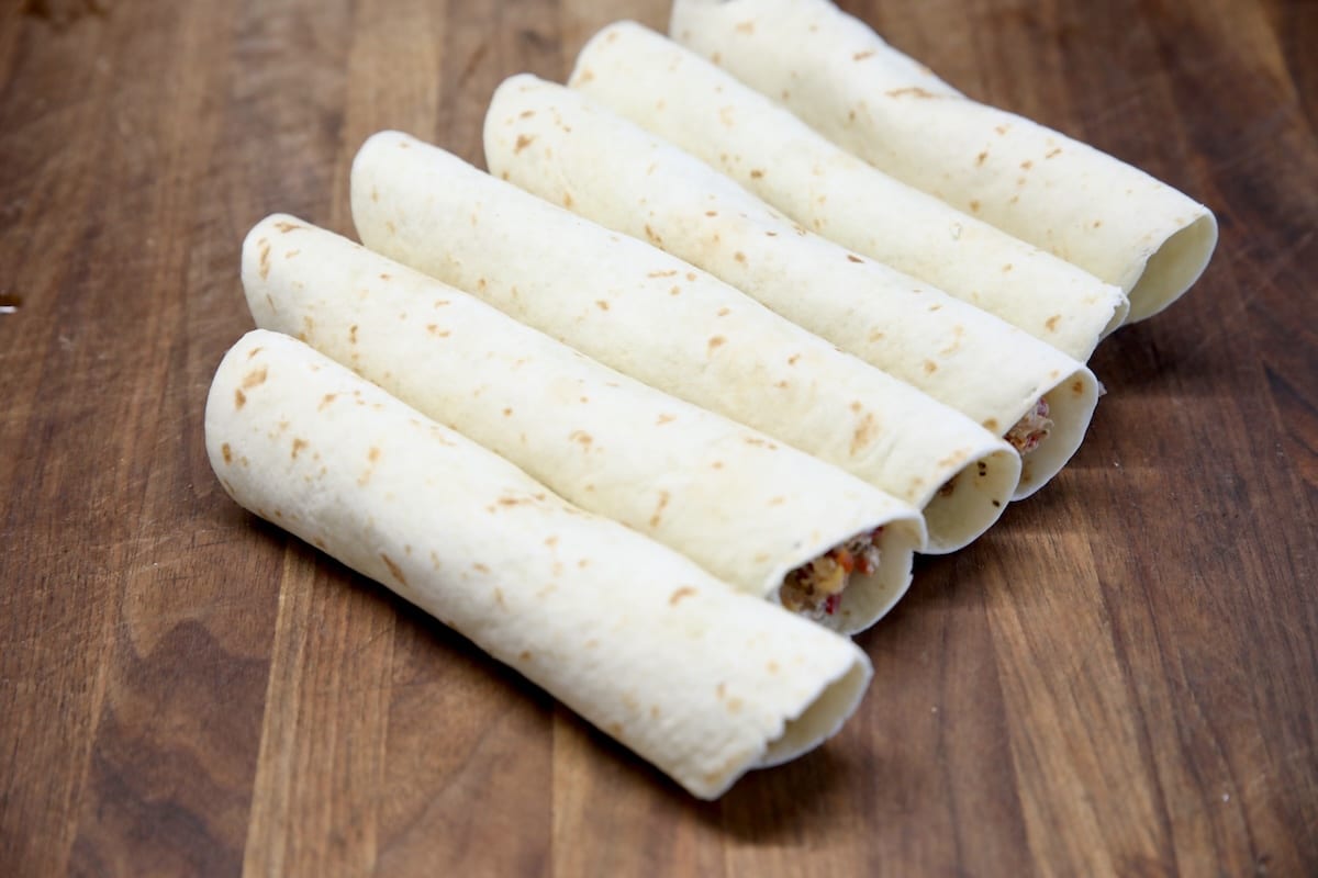 Uncooked taquitos on a cutting board.