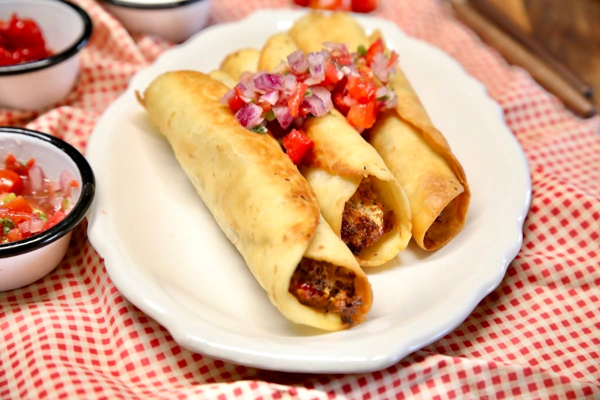 3 brisket popper taquitos on a plate with pico de gallo.