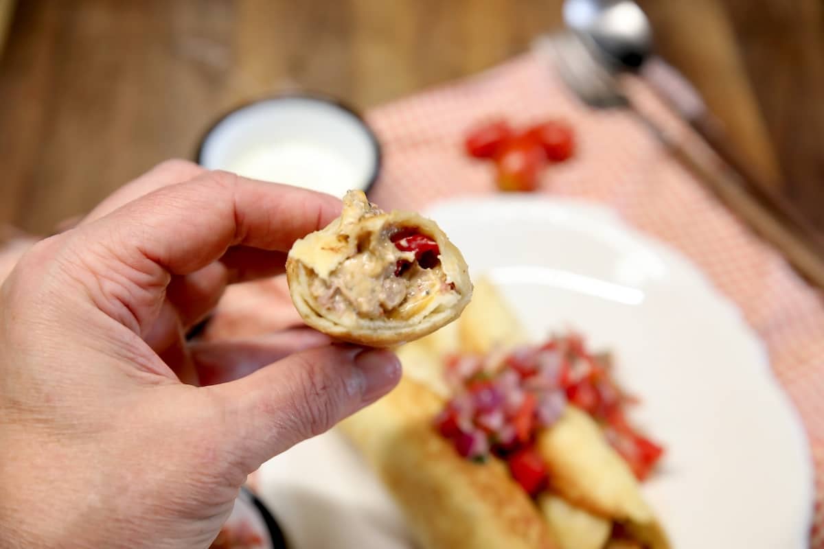 Hand holding taquito with filling showing.