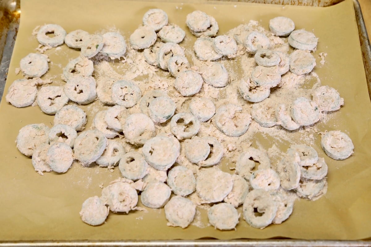Sliced jalapenos with coating on a baking sheet ready to fry.