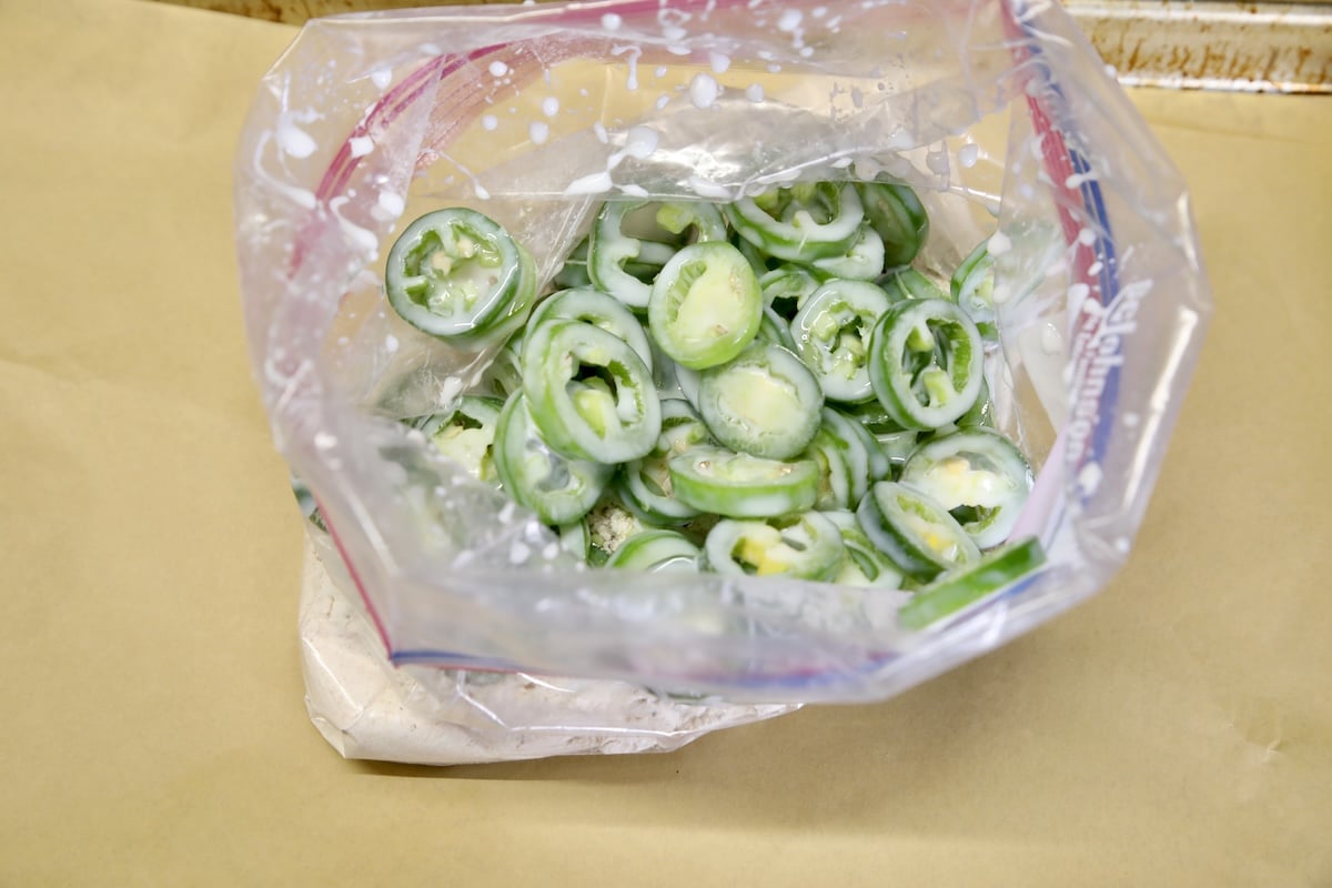 Coating jalapenos in seasoned flour in a ziploc bag.