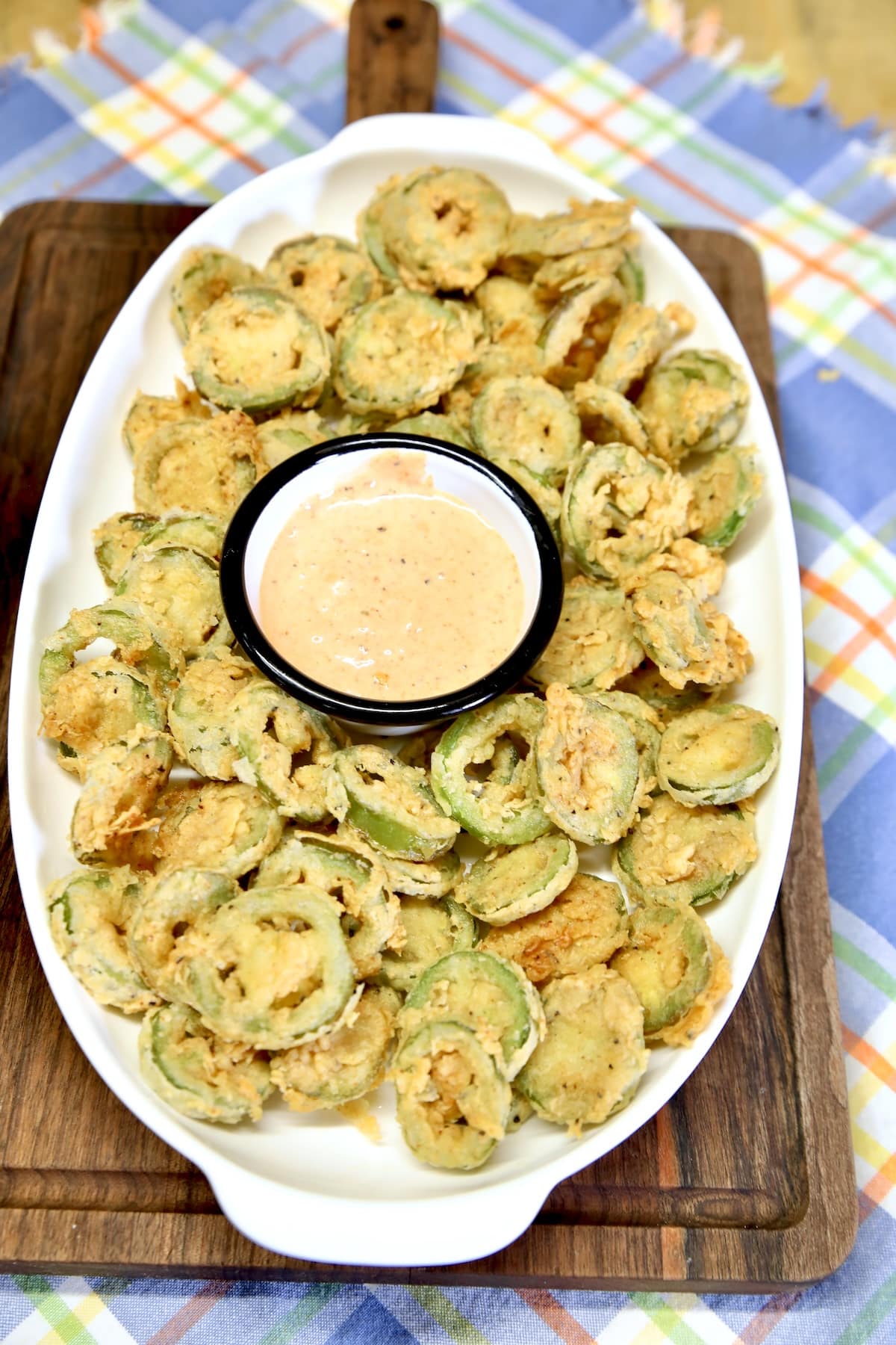 Platter of jalapeno slices with blooming onion sauce in a cup.