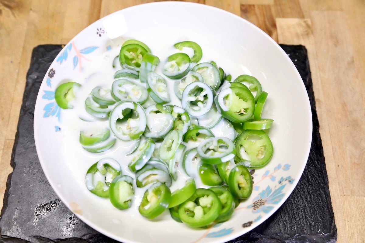 sliced jalapenos in a bowl with buttermilk.