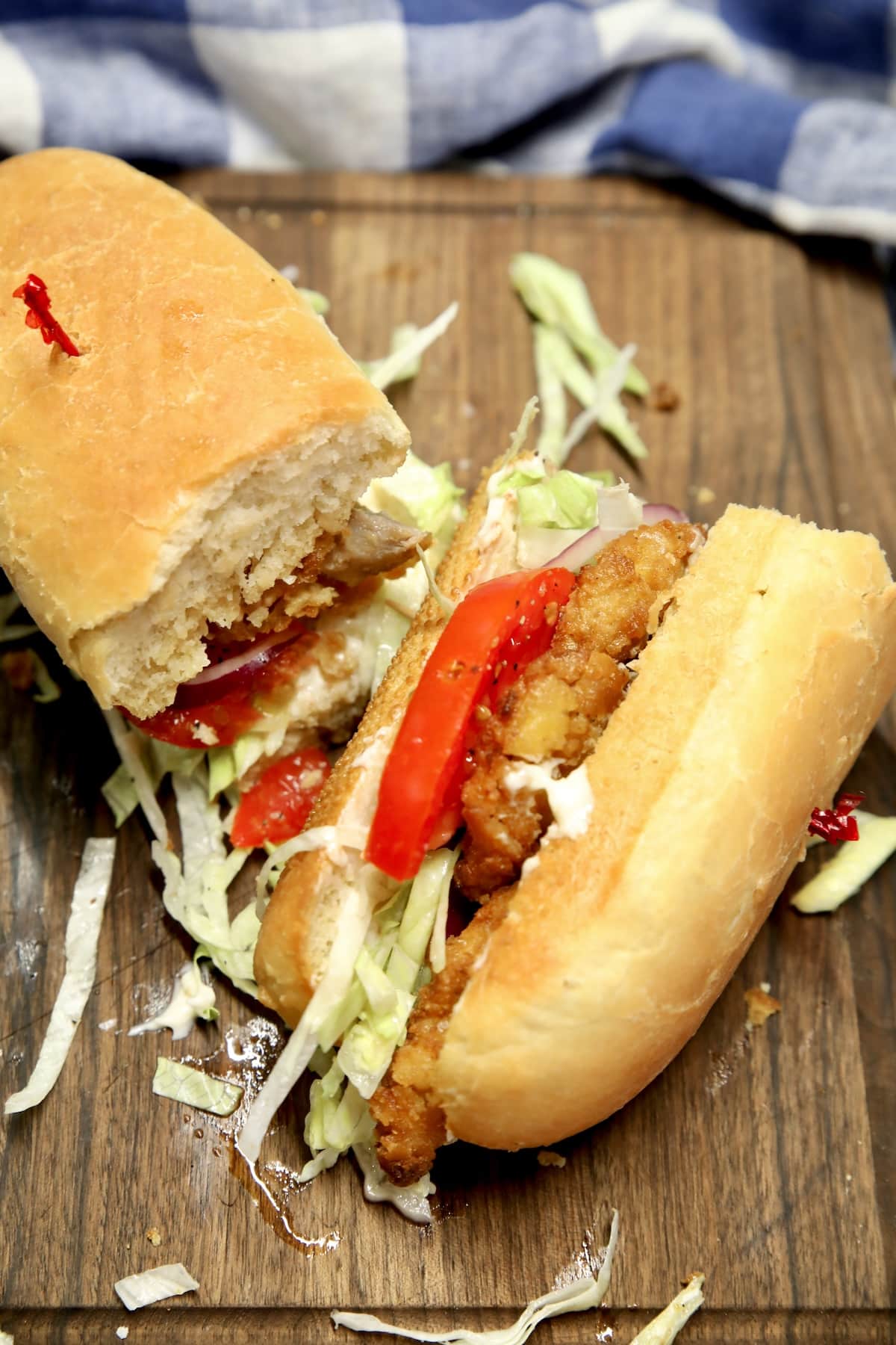 Crispy pork sandwich cut in half on a board.