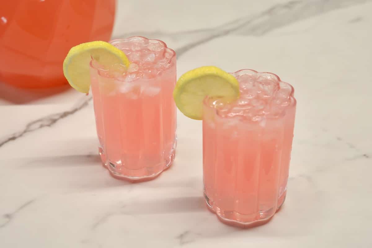 2 pink cocktails in glasses with lemon slices.