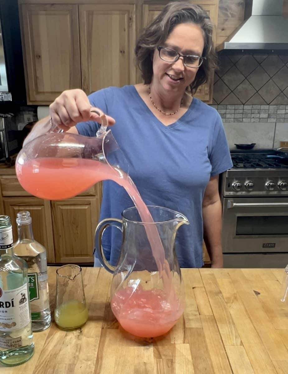 Pouring pink lemonade into a pitcher.