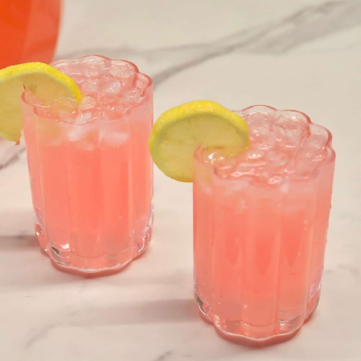 Pink punch in 2 glasses with lemon garnish.