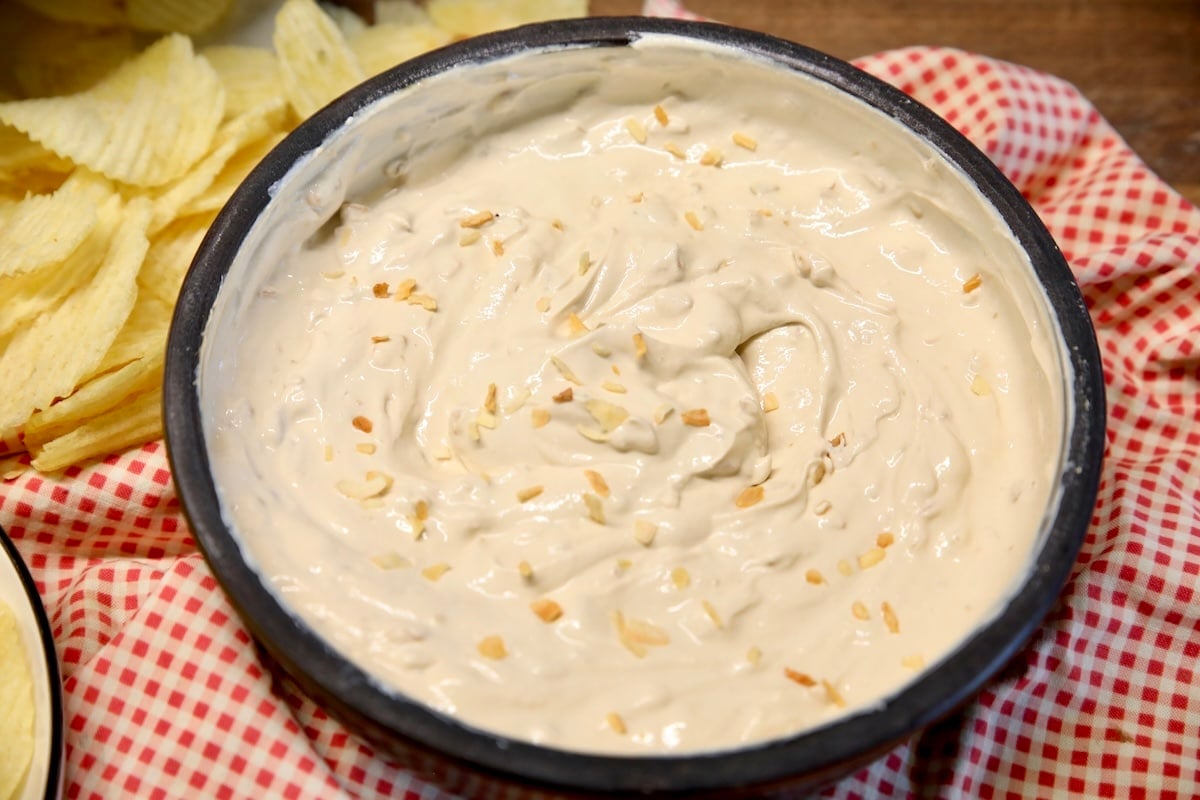 Bowl of Onion dip on a red check napkin with chips.
