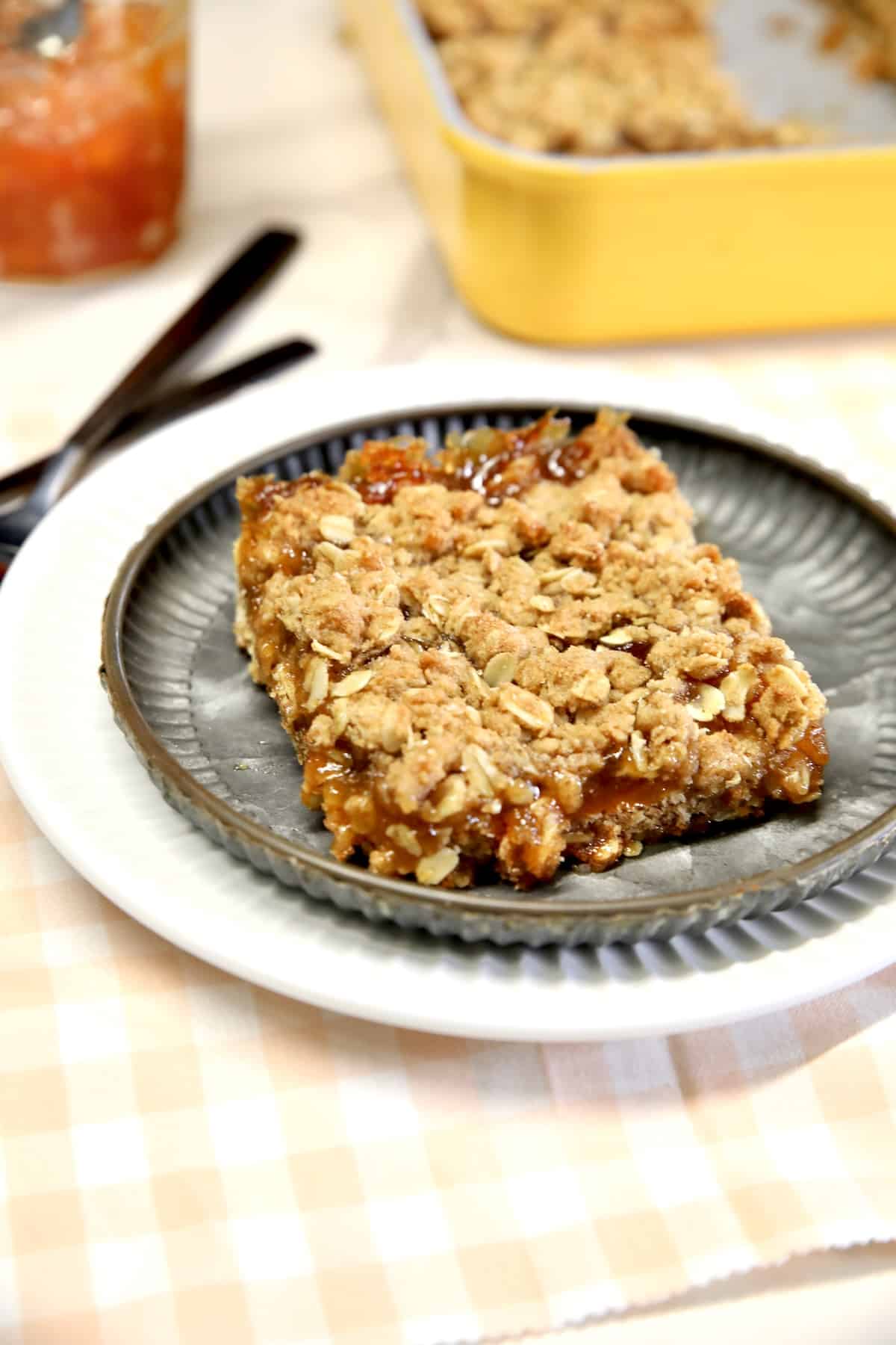 Peach oat bars on a plate, pan of bars, jar of preserves.