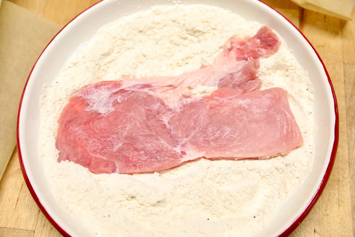 Dredging pork chop in flour.