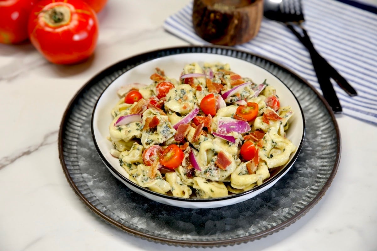 Pasta salad with cheese tortellini, pesto, bacon and tomatoes. Bowl of tortellini salad with tomatoes and bacon.