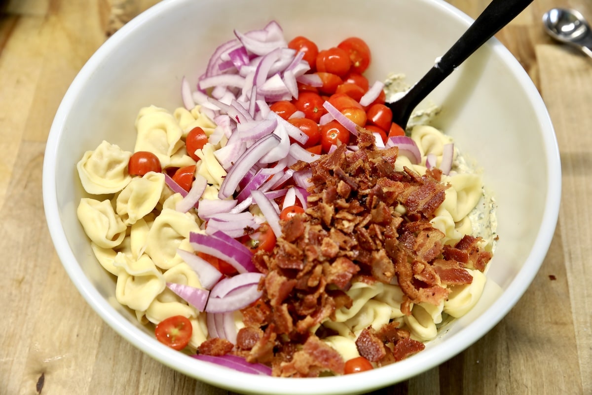 Making tortellini salad with bacon, tomatoes, red onion.