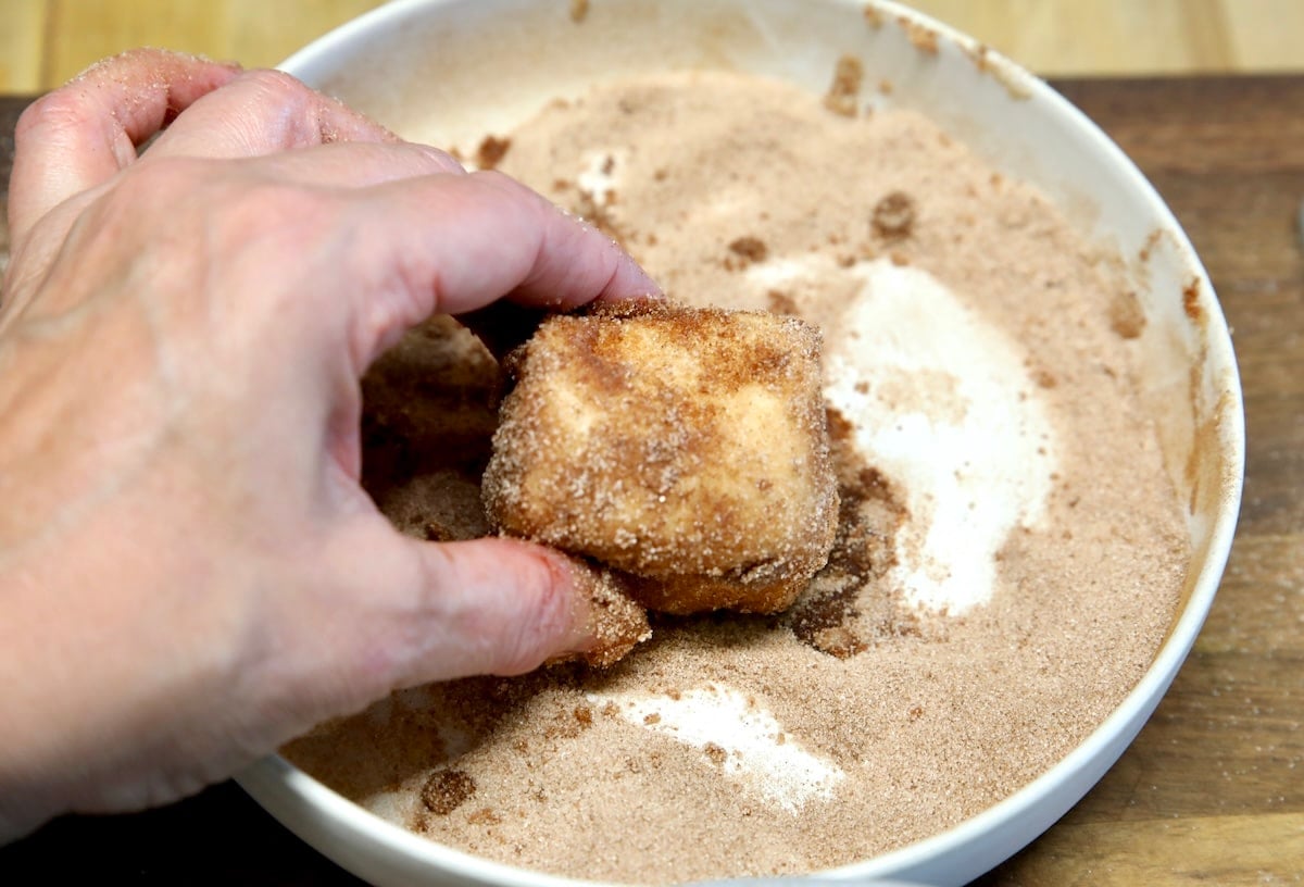 Rolling butter dipped croissant in cinnamon sugar.