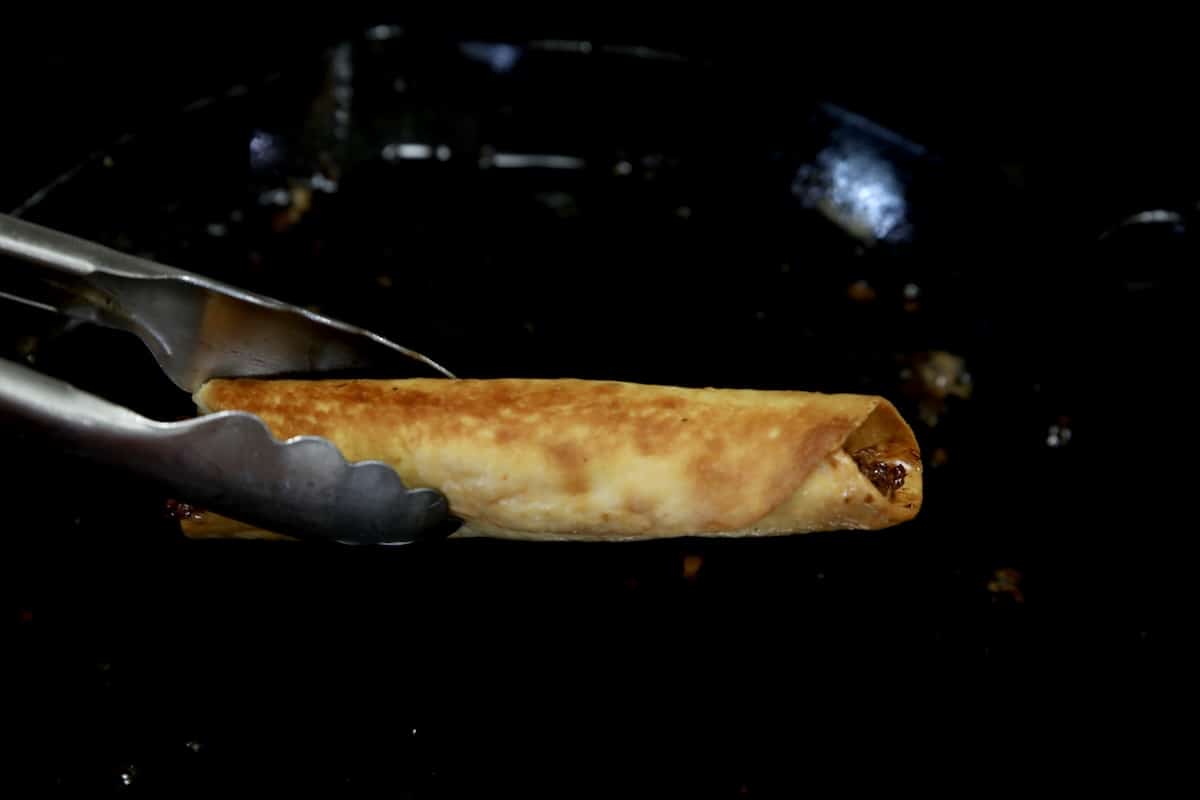 Fried taquito with tongs.