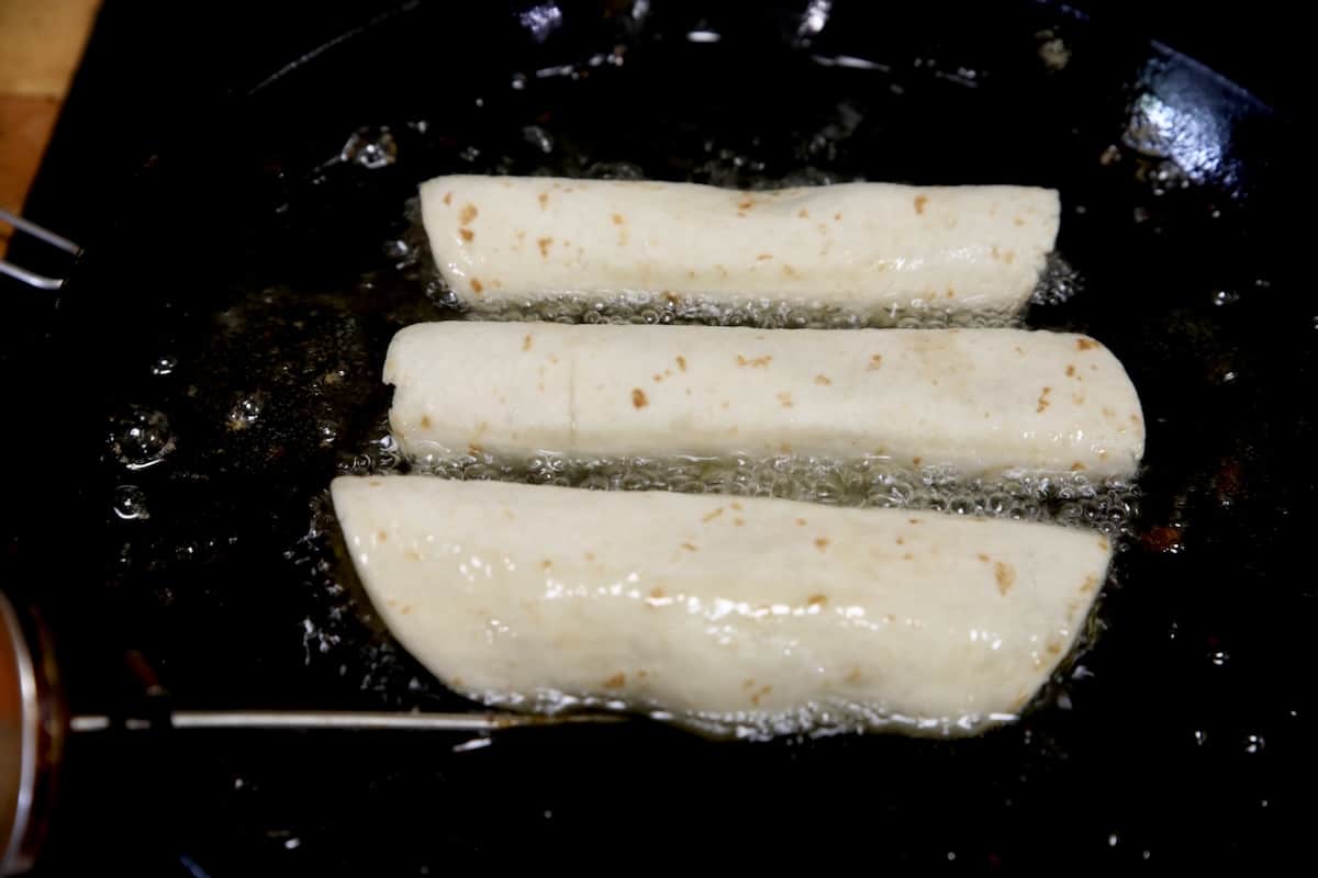 Frying taquitos in a skillet.