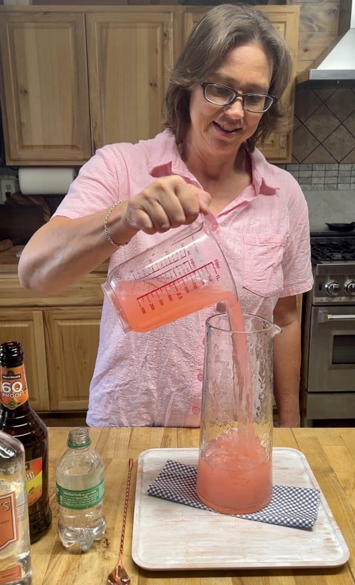 Pouring pink lemonade into a pitcher.