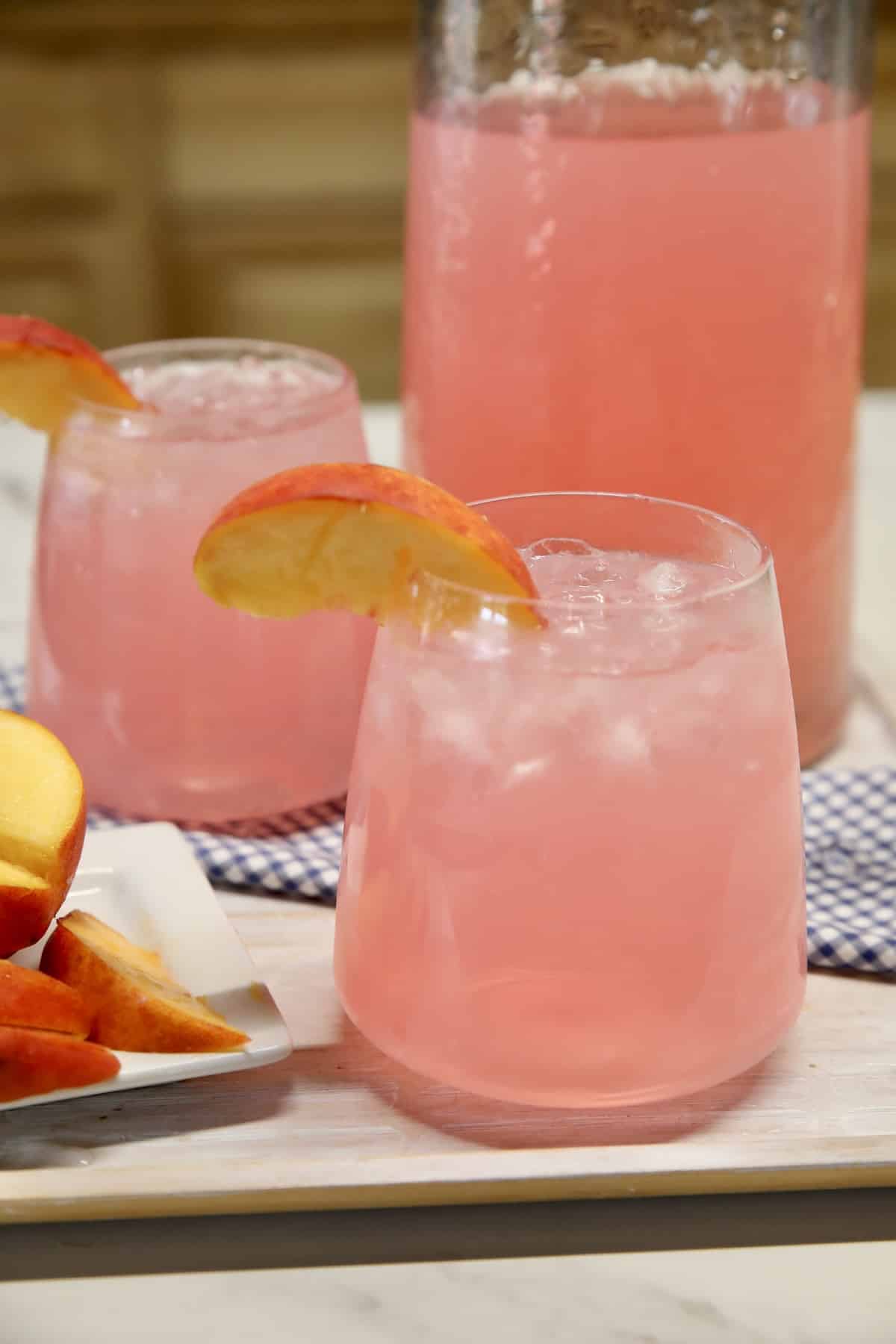 Pitcher and 2 wine glasses with peach vodka pink lemonade cocktail.