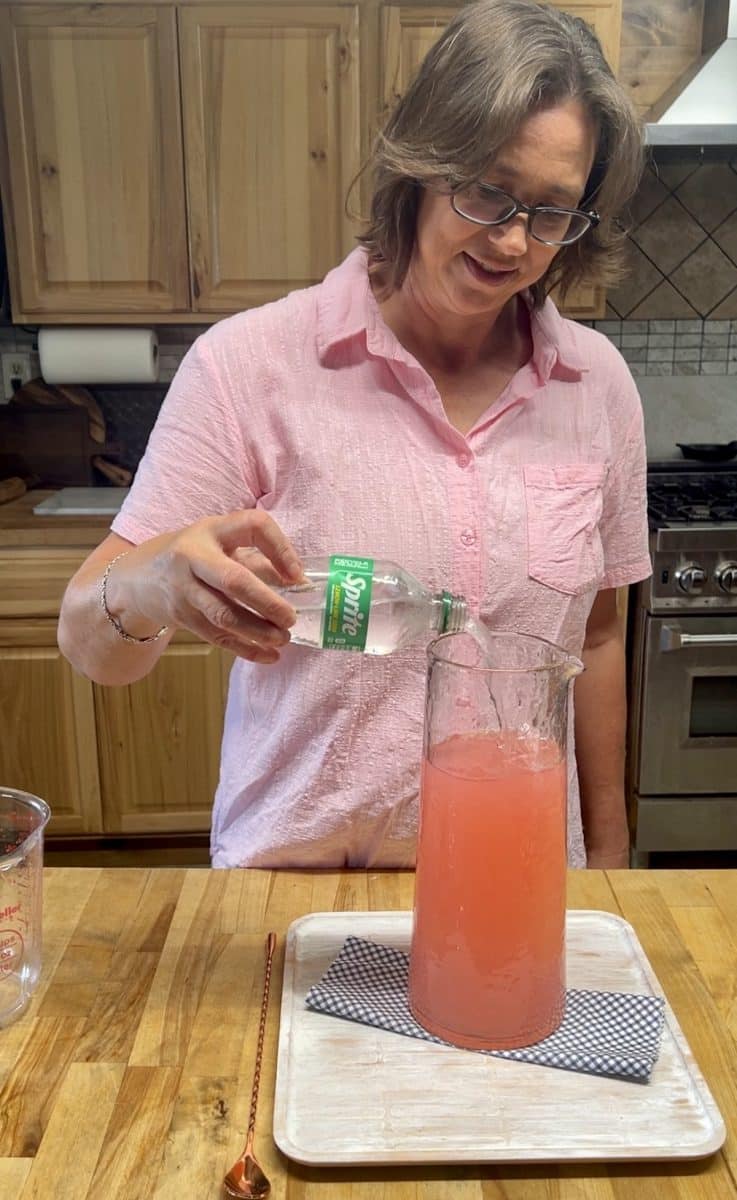 Pouring sprite into a pitcher of punch.