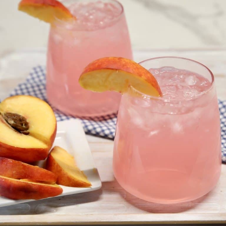 Peach vodka lemonade in 2 stemless wine glasses - peach garnish.