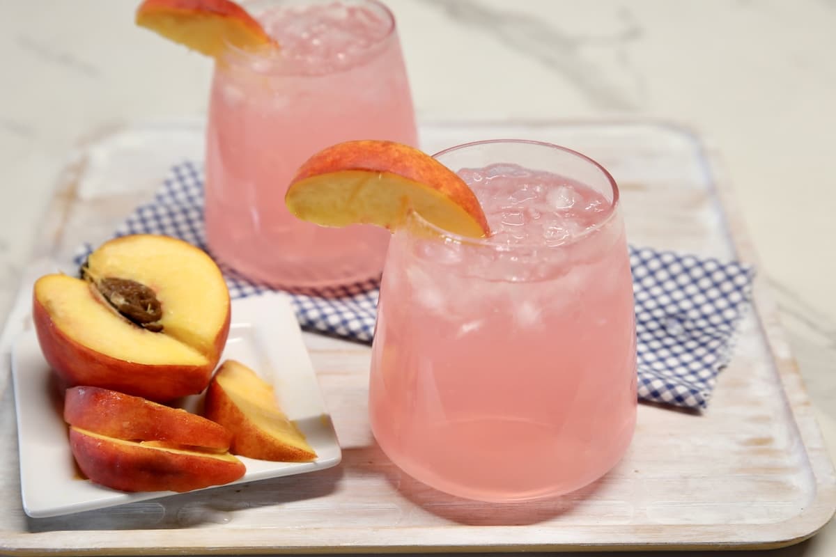 2 glasses of peach vodka lemonade with fresh peach garnish.