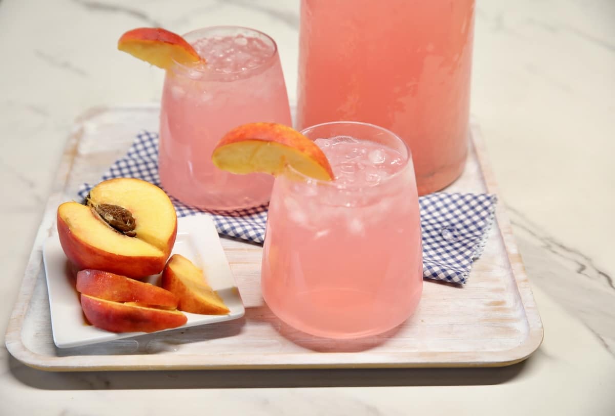 Peach vodka lemonade punch. Peach vodka lemonade in 2 glasses with pitcher, sliced peach.