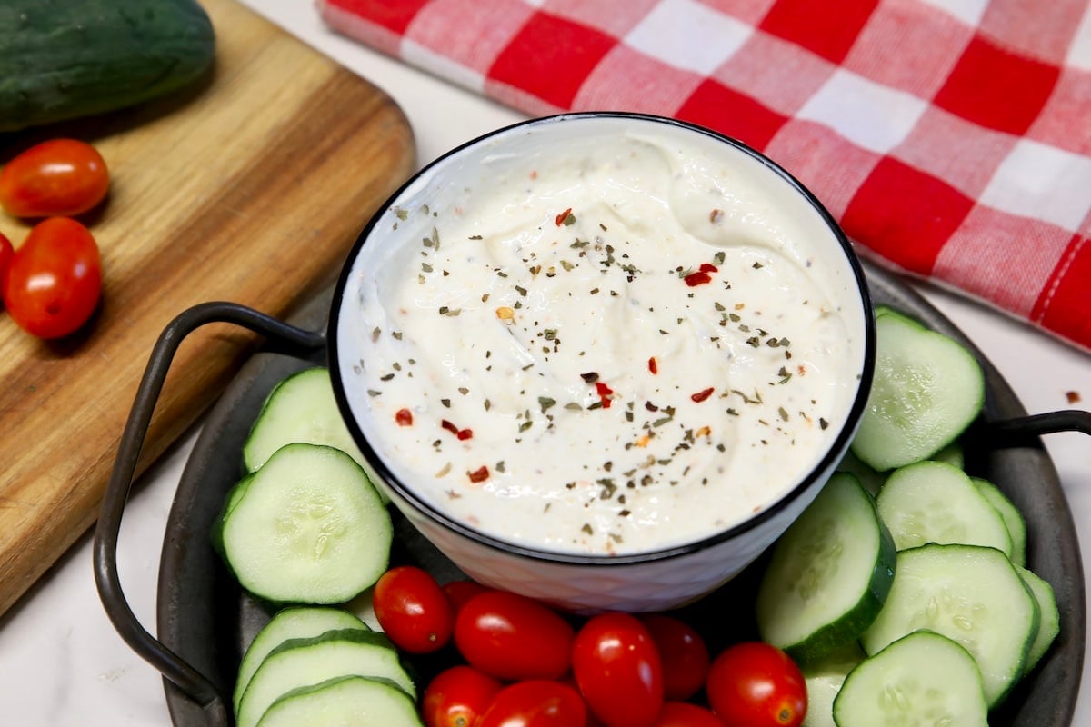 Bowl of greek yogurt veggie dip with cucumber slices and grape tomatoes.