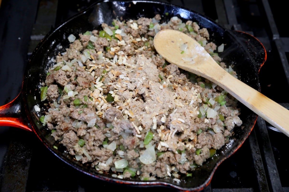 Adding onion soup mix to ground beef skillet.