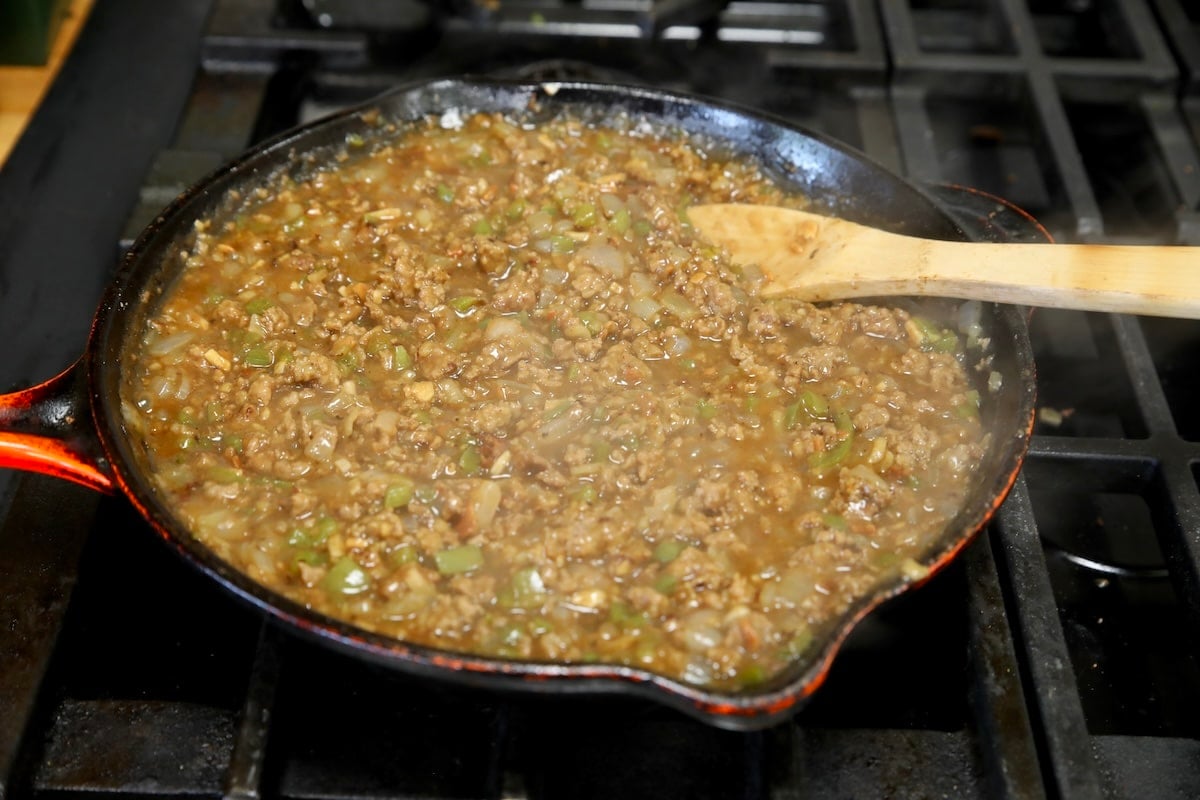 Simmering sloppy joes filling in a skillet with spoon.